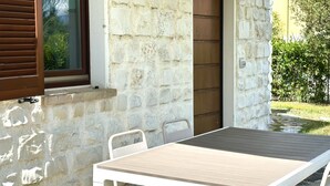 A stone exterior wall with a wooden door, a window with brown shutters, and a table with chairs outside. - M375 - Marcelli, two-room apartment with garden in a residence with swimming poo (Numana)