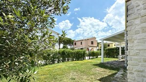 A garden with a stone wall, a white building, and a pink house in the background. - M375 - Marcelli, two-room apartment with garden in a residence with swimming poo (Numana)