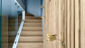 Een trap met een glazen leuning en een houten muur met een messing deurklink.
