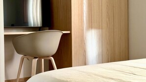 Een moderne kamer met een bed, een aan een houten wand bevestigde televisie en een witte stoel.