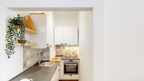 Eine kleine Küche mit Spüle, Backofen und einem Holzregal mit einer Pflanze.