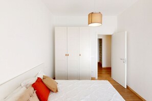 A bedroom with a bed, white wardrobe, and a hallway leading to another room.