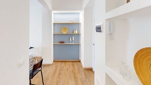 Ein schmaler Flur mit Holzboden, einem Schreibtisch mit Stuhl und einer blauen Wand mit Regalen, die verschiedene Gegenstände beherbergen.