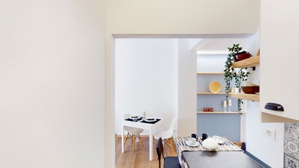 Eine moderne Küche mit weißen Schränken, ein Essbereich mit Tisch und Stühlen sowie ein Regal mit Dekoration.
