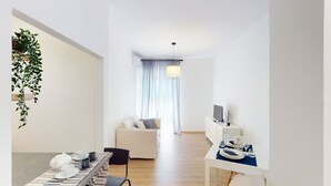 Ein modernes Wohnzimmer mit einer Couch, einem Esstisch mit Stühlen, einem Fernseher und einer hängenden Pflanze.