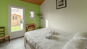 A bedroom with a bed, a wooden chair, a small table, a door leading outside, and a framed picture on the wall. - La Merisolle - 850m mer - Wifi (Pornic)