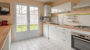 A kitchen with white cabinets, a dishwasher, a stove, and a window with a view of the outdoors. - La Merisolle - 850m mer - Wifi (Pornic)