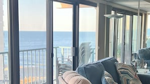 Habitación con un amplio ventanal corredero que da a un balcón con vistas al océano. Hay un sofá y una silla dentro de la habitación.