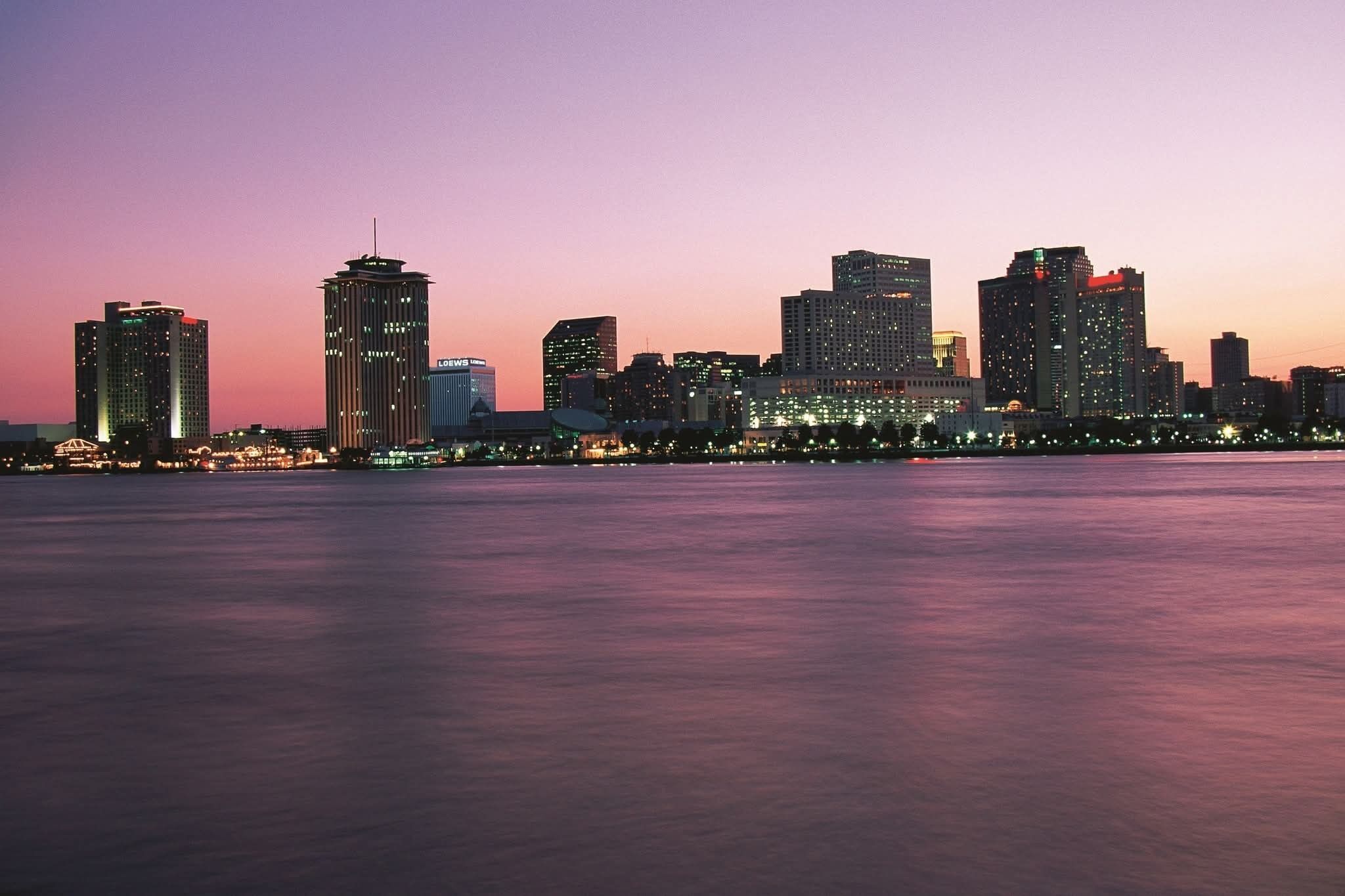 A city skyline at dusk with illuminated buildings across a body of water.