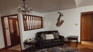 Ett vardagsrum med en svart lädersoffa, en mönstrad matta, en gitarr som hänger på väggen, ett litet bord i trä och en kristallkrona.