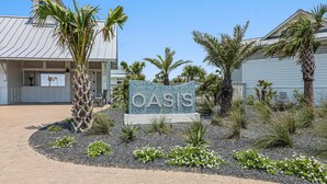 A sign with the word "OASIS" surrounded by a landscaped area with palm trees and small plants.