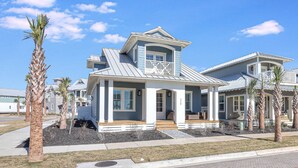 A two-story house with a covered porch, a balcony, and a well-maintained lawn with palm trees.