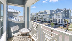A balcony with a view of a row of houses, a table, and two chairs.