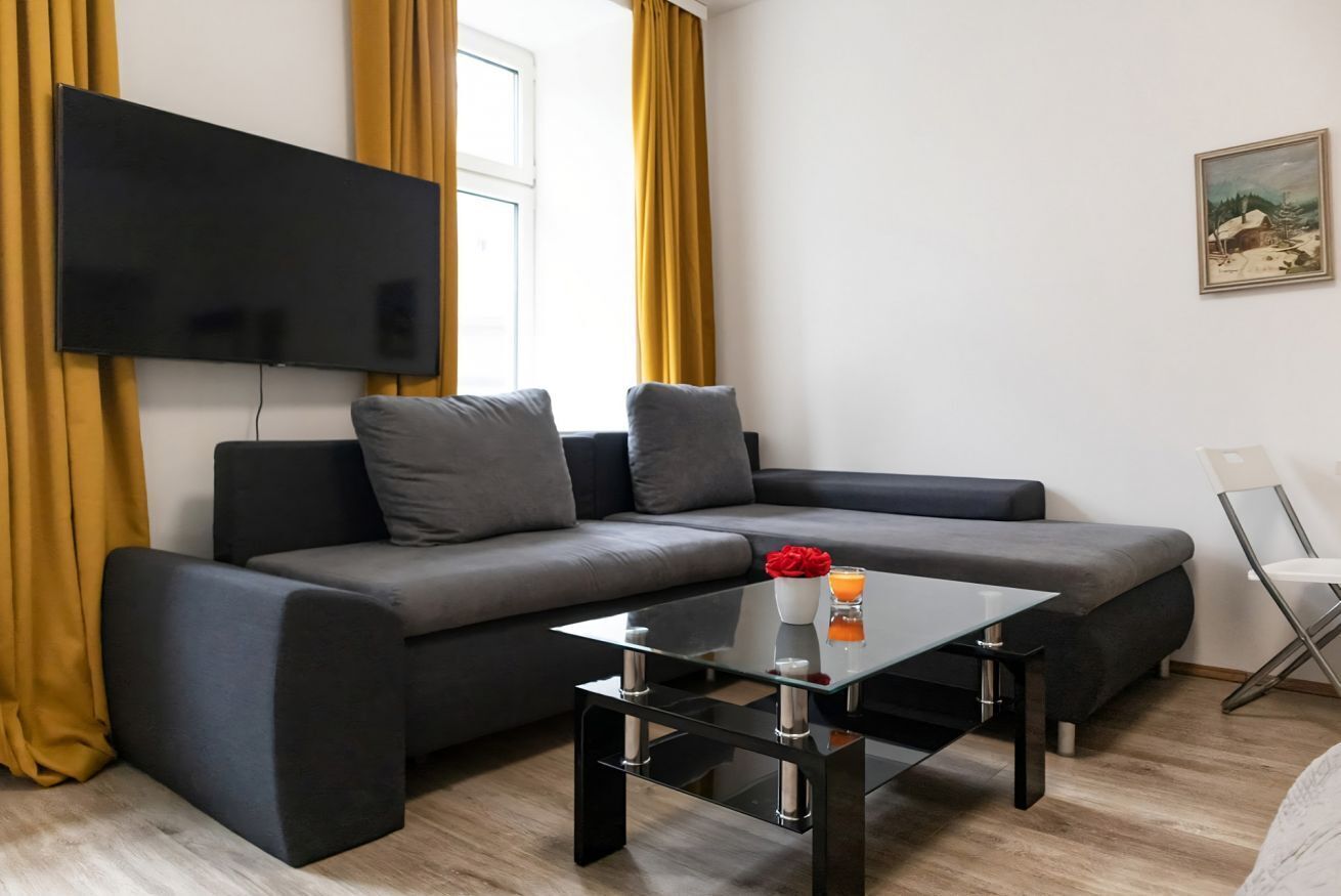 Ein modernes Wohnzimmer mit einer Eckcouch, einem Glastisch, einem Flachbildfernseher und einem Gemälde an der Wand.