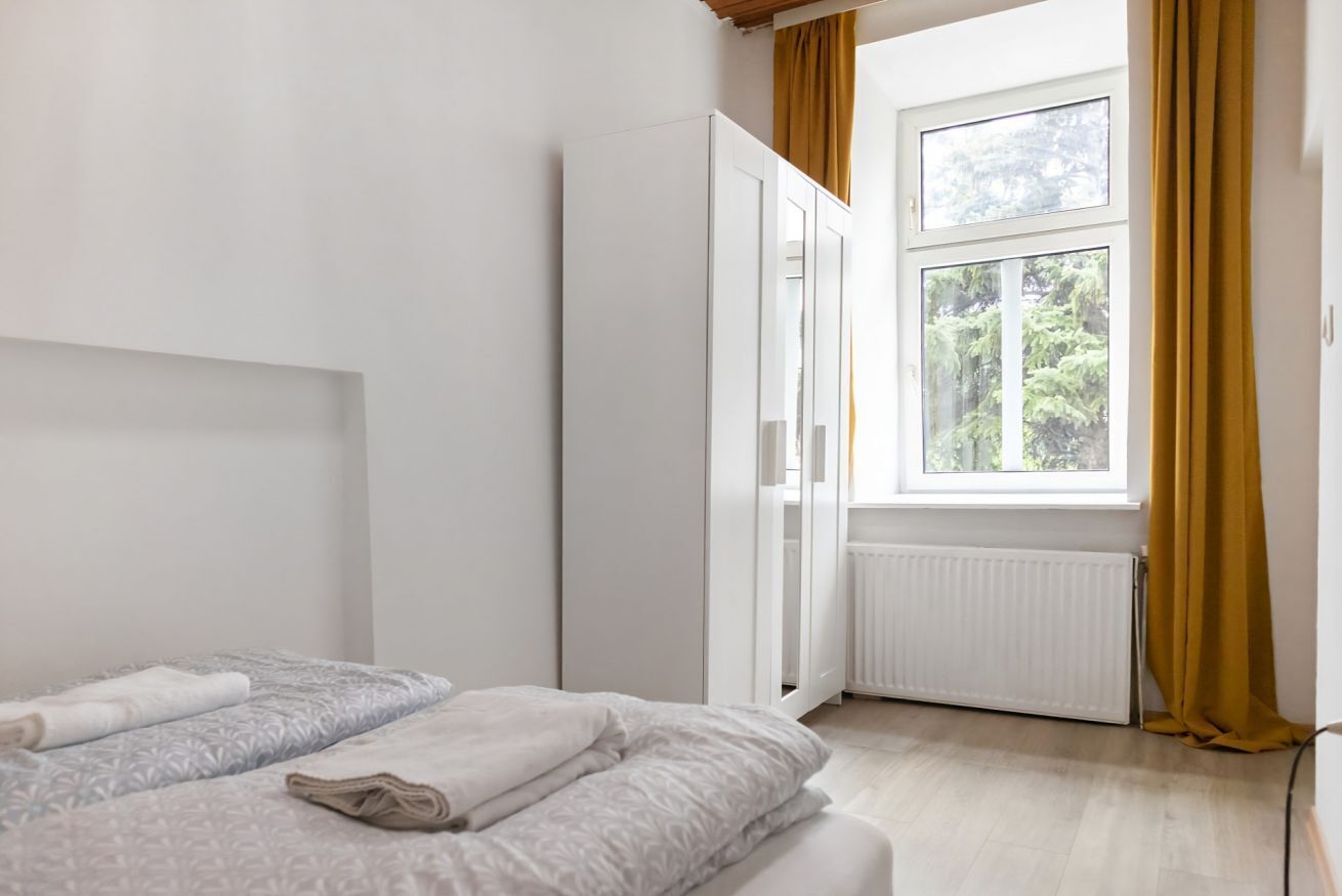 A bedroom with a bed, a wardrobe, a window with curtains, and a radiator.