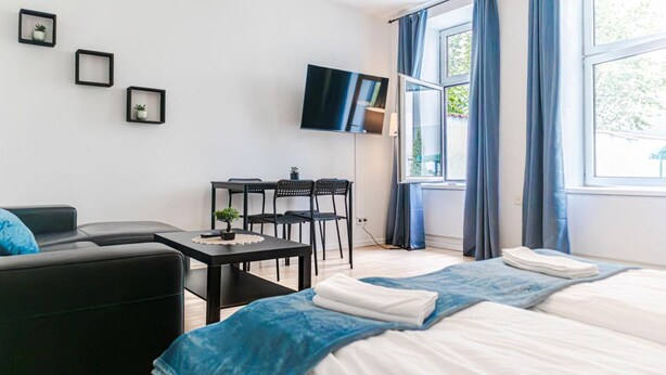 A hotel room with a bed, a desk, two chairs, a TV, and a window with curtains. - Budget City Living: 1BR w/ Private Garden (Wien)