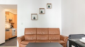 A modern living room with a leather sofa, a dining table, and a kitchen in the background.