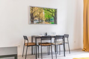 Uma sala de jantar com uma mesa posta para quatro pessoas, cadeiras e um quadro emoldurado acima da mesa.
