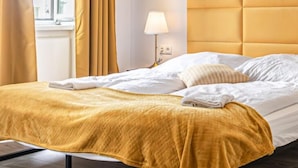 A neatly made bed with a yellow headboard, white bedding, and a lamp on a bedside table.