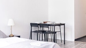 A hotel room with a bed, a table with chairs, a lamp, and a small table with a bowl and a spoon. - Charming 1BR Apt. Near U6 Station am Schöpfwerk (Vienna)