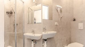 A bathroom with a glass-enclosed shower, two sinks, a toilet, and a hairdryer mounted on the wall. - Charming 1BR Apt. Near U6 Station am Schöpfwerk (Vienna)