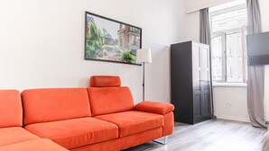 A modern living room with a sectional sofa, a flat-screen TV, a cabinet, and a window with curtains. - Charming 1BR Apt. Near U6 Station am Schöpfwerk (Vienna)