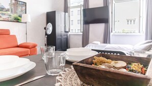 A hotel room with a dining table set with plates, glasses, and a wooden bowl of food.