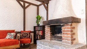 Ein gemütlicher Raum mit Kamin aus Backsteinen, einem roten Sofa, einem hölzernen Stuhl und einem Bücherregal.