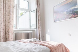 Une chambre à coucher avec un lit, un radiateur, une fenêtre avec des rideaux et un tableau accroché au mur.