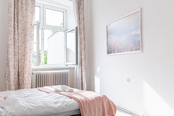 A bedroom with a bed, a window with curtains, a radiator, and a wall-mounted picture.