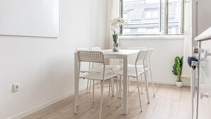 Une table à manger blanche avec quatre chaises, une plante en pot et une fenêtre avec des rideaux.