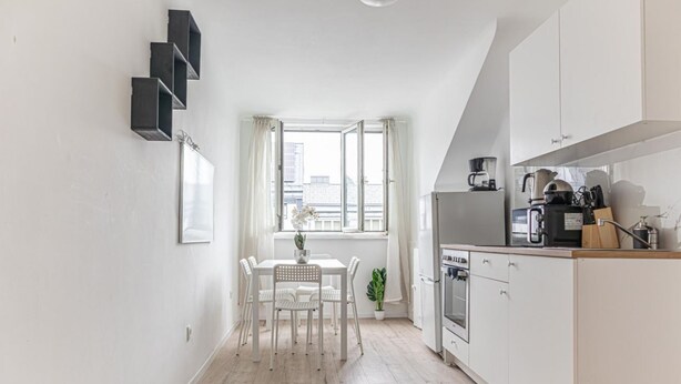 Une cuisine moderne avec des meubles blancs, une table à manger avec des chaises et une fenêtre avec des rideaux.