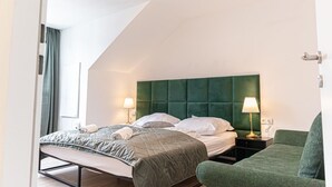 Une chambre moderne avec une tête de lit verte, un lit recouvert de draps blancs, deux lampes de chevet et un fauteuil vert.