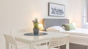 A hotel room with a bed, a framed cityscape picture, a table with chairs, and a potted plant.