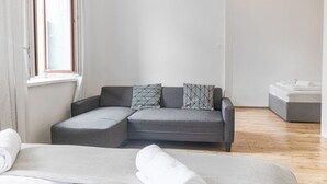 A modern, minimalist room with a grey sofa, a bed, and a window with curtains.