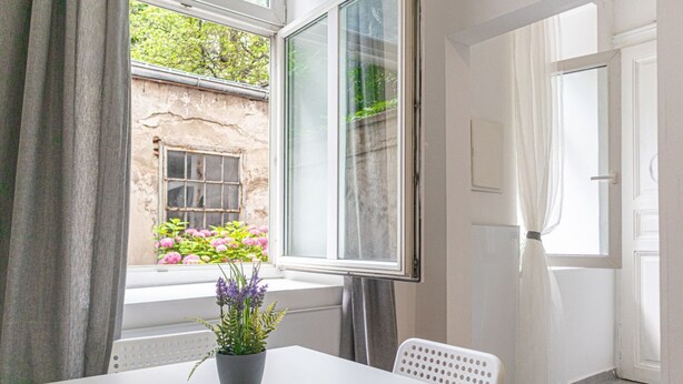 Una habitación con ventana, una mesa blanca, una planta en maceta y una silla blanca.