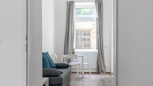 Una habitación con un sofá gris, una mesita, dos sillas y una ventana con cortinas.