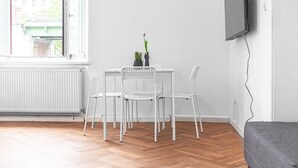 Une pièce avec un radiateur blanc, une table avec deux chaises, une plante en pot et un téléviseur fixé au mur.