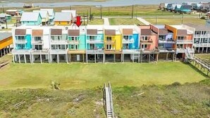 Um edifício de vários andares com telhado plano, um pátio central e vista para o mar ao fundo.