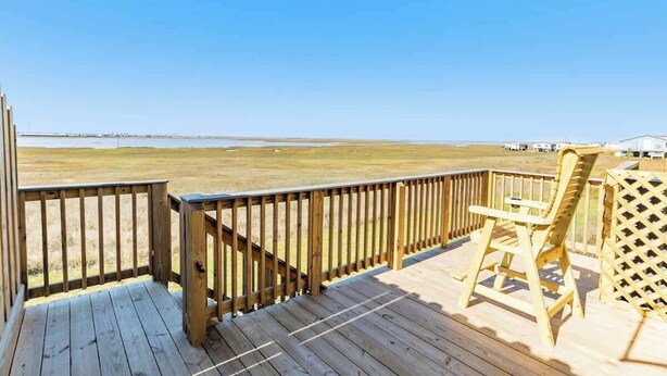 Une terrasse en bois offrant une vue sur un paysage plat et sur une étendue d’eau lointaine.