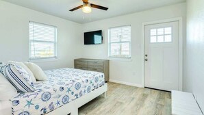 Une chambre à coucher avec un lit, un ventilateur de plafond, une télévision et deux fenêtres.
