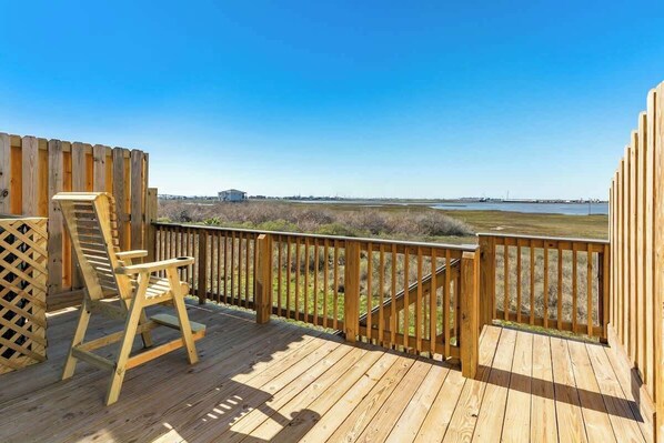 A wooden deck with a wooden chair and a lattice panel, overlooking a coastal landscape.