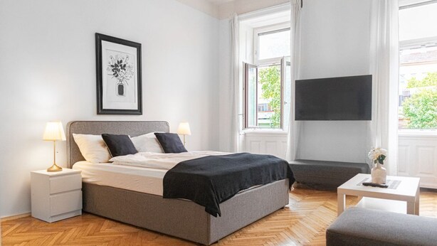 A bedroom with a bed, bedside tables, a TV, and a window.