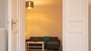 A hallway with a white door, a white radiator, a brown sofa with a green pillow, and a white coffee table with a plant.