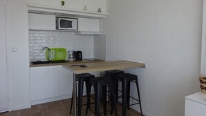 Kompakti keittiö, jossa on mikroaaltouuni, pesuallas ja baarituolit.