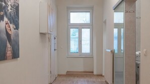 Ein Flur mit Holzboden, einem Fenster mit Jalousien, einer Tür und einer Duschkabine aus Glas.
