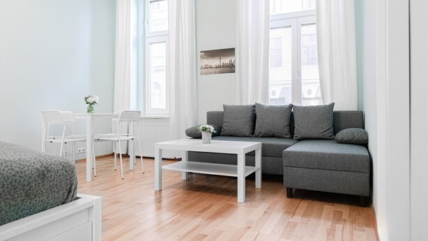 Ein modernes Wohnzimmer mit grauem Sofa, weißem Couchtisch und weißen Stühlen.