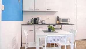Een kleine keuken met witte kastjes, een magnetron, een koffiezetapparaat en een potplant op het aanrecht.
