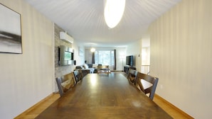 Een eetgedeelte met een lange houten tafel, stoelen, een bank en een televisie.
