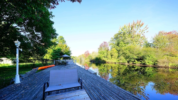 Een houten terras dat uitstelt over een rustige rivier, omgeven door weelderige begroeiing en bomen.
